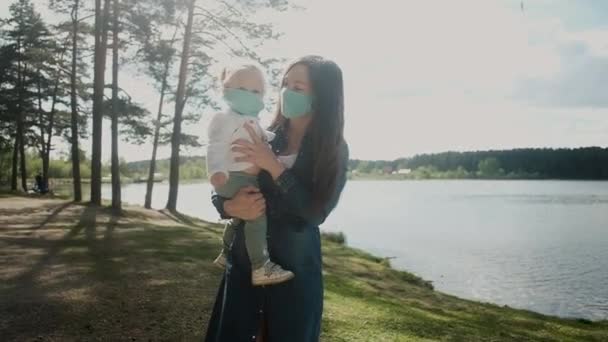 年轻的母亲抱着一个小女儿。夏天在湖边的公园里散步.科罗纳威斯大流行病Covid 19 。检疫期间的积极生活方式的概念。照料、保护 — 图库视频影像