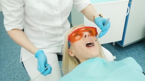 Dentiste tenant des instruments dentaires dans la bouche d'une cliente. Le dentiste tient la sonde dans une main et l'embout buccal dans l'autre. Le médecin vérifie l'état des dents. armoire — Video