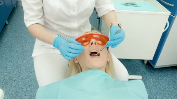 Dentist holding dental instruments in the mouth of a woman client. The dentist holds the probe in one hand and the mouthpiece in the other. The doctor checks the condition of the teeth. cabinet — Stock Video