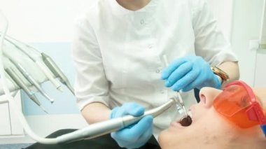 Dişçi kadın elleri steril eldivenlerle hastayı matkap kullanarak tedavi ediyor. Kadın müşteriye diş delme konusunda uzman stomatolog. Bakım, tedavi. Ama bahşişler...