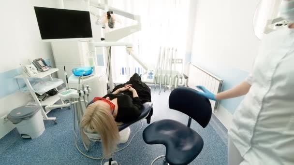 Dentista sosteniendo instrumentos dentales en la boca de una mujer cliente. El dentista sostiene la sonda en una mano y la boquilla en la otra. El médico comprueba el estado de los dientes. gabinete — Vídeo de stock