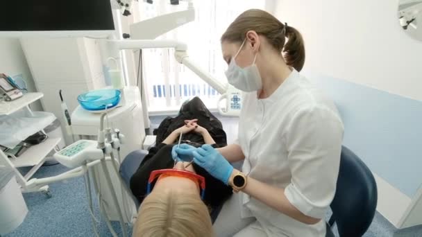 Dentysta trzymający instrumenty dentystyczne w ustach klientki. Dentysta trzyma sondę w jednej ręce, a ustnik w drugiej. Lekarz bada stan zębów. szafka — Wideo stockowe