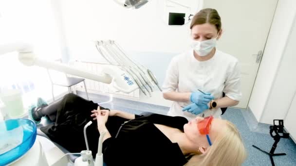 Dişçi, dişçi aletlerini kadın bir müşterinin ağzında tutuyor. Dişçi bir elinde sondayı, diğer elinde de sözlüğü tutuyor. Doktor dişlerin durumunu kontrol ediyor. dolap — Stok video