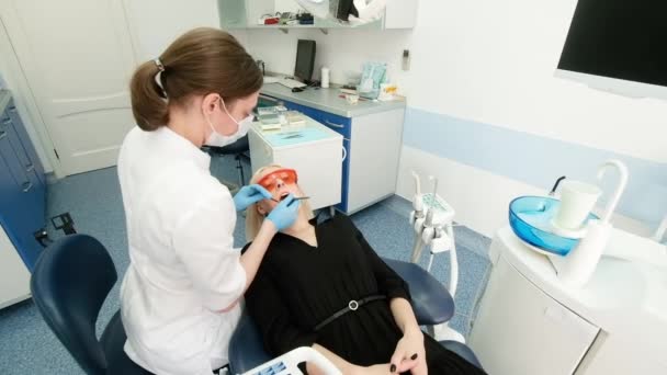 Tandläkare som håller dentala instrument i munnen på en kvinnlig klient. Tandläkaren håller sonden i ena handen och munstycket i den andra. Läkaren kontrollerar tändernas tillstånd. kabinett — Stockvideo