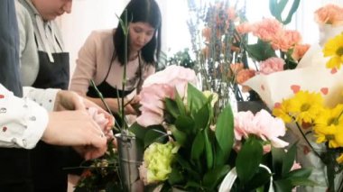 Yakın plan. Çiçek tasarımı yapan kadın çiçekçiler. Genç profesyoneller tarafından güzel çiçek buketleri yapma pratiği. Çiçekçide çalışıyorum. Tatil hazırlığı, düğün, yıldönümü