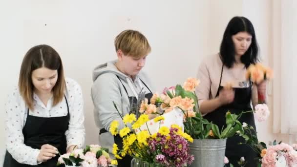 Çiçekçi bir grup kadın çiçek tasarımı yapıyor. Grup olarak. Genç profesyoneller tarafından güzel çiçek buketleri yapma pratiği. Çiçekçide çalışıyorum. Tatil için hazırlık, düğün, yıldönümü — Stok video