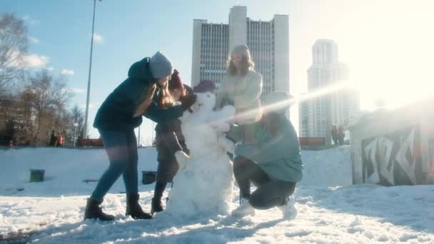 Quatro raparigas na cidade fazem um boneco de neve. Há muito tempo que não te via. Eles brincam, se divertem em um dia nevado no parque. Conceito de amizade. Passeie. Inverno. Colegas, colegas — Vídeo de Stock