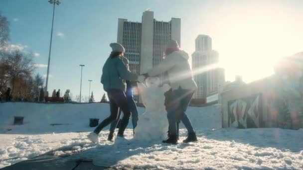 Quatro raparigas estão a fazer um boneco de neve na cidade. Há muito tempo que não te via. Eles brincam, se divertem em um dia nevado no parque. Conceito de amizade. Passeie. Inverno. Colegas, colegas — Vídeo de Stock