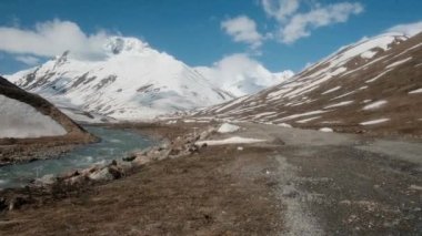Dağlık arazide, karlı bir dağın arka planına çarpan off-road aracı. Kayalık arazi. Macera, seyahat. Çakıl taşı yolu. Engelleri aşmak, aşırı, tatil