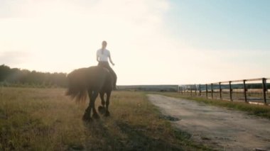 Arenada siyah zarif bir ata binen kadın jokey. Binicilik bahçesi. Aktif yaşam tarzı konsepti. Jokey. Spor. Hafta sonu binicilik kulübünde. Yaz günbatımı. Yavaş hareket et