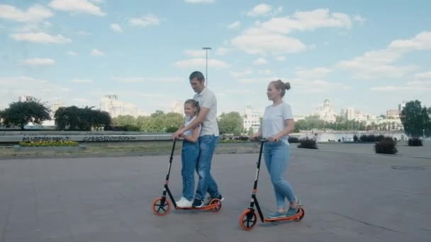 Familia joven feliz montar scooters. Concepto de ocio para la juventud. Paseo de fin de semana en la ciudad. Mamá feliz, papá, hija se están divirtiendo en el parque. Estilo de vida activo. El amor es cuidar. — Vídeo de stock