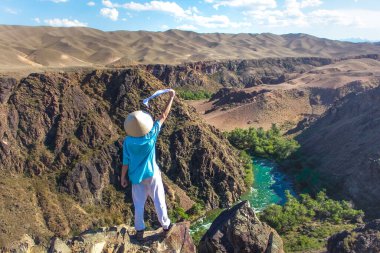 Asyalı şapkalı bir adam kanyona ve nehre bakıyor.