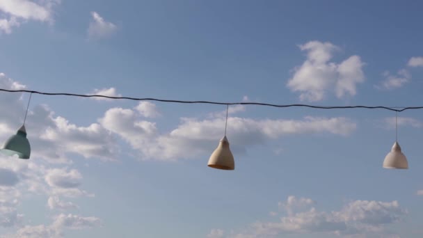 Lámpások a kötélen. Díszlámpák kék égbolttal. Elektromos vezetékre akasztva. — Stock videók