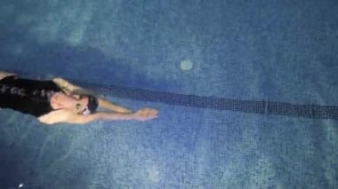 Sporcu kadın kapalı havuzda kelebek tekniği yüzüyor ve olimpiyat oyunlarına hazırlanıyor. Su havuzuna dal.