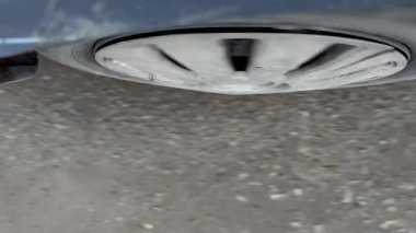 Asfalt üzerinde dönen yakın çekimli araba tekerleği, dağınık yapraklar ve toprak ile bulanık hareket, görünür jant kapağı ve kenar