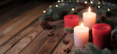 Candles on a rustic wooden table with copy space. Tranquil Christmas mood with burning Advent candleflames and fir branches