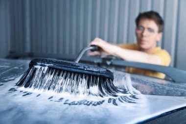 Arabayı fırça ve köpükle temizleyen bir adam. Aktif yetişkin işleri yapıyor..