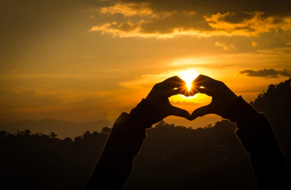 Silhouettes main en forme de coeur avec des couchers de soleil et le ciel orange — Photo