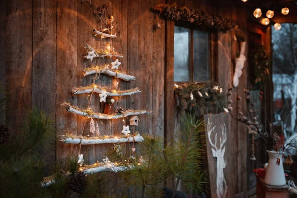 Árvore de Natal em um fundo de madeira rústico no terraço às luzes da noite são iluminados. Decorações de Natal com suas próprias mãos em um estilo escandinavo rústico. — Fotografia de Stock