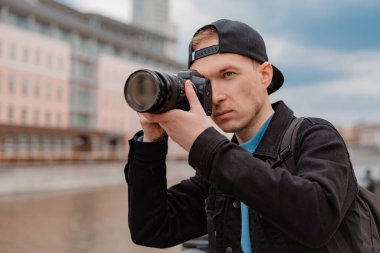Genç adam siyah şapka, kamera merkezli adam şehir merkezinde fotoğraf çekiyor..