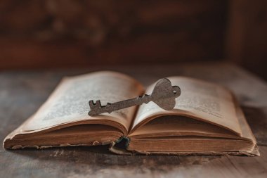 Dekoratif ahşap bir anahtar, karanlık bir arka planda eski bir kitabın üzerinde duruyor.