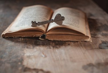 Dekoratif ahşap bir anahtar, karanlık bir arka planda eski bir kitabın üzerinde duruyor.