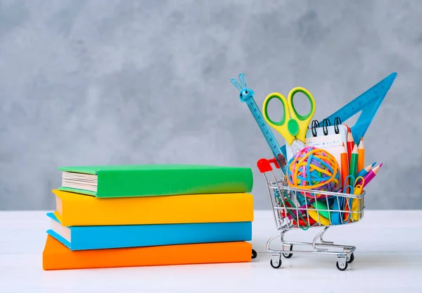 Colorful school supplies in the shopping basket on a gray background with a copy of the text space. A stack of books with colorful covers.