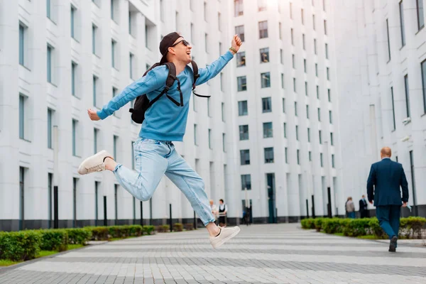 Joven chico con estilo en la ropa azul salta en el fondo de un edificio moderno blanco. — Foto de Stock