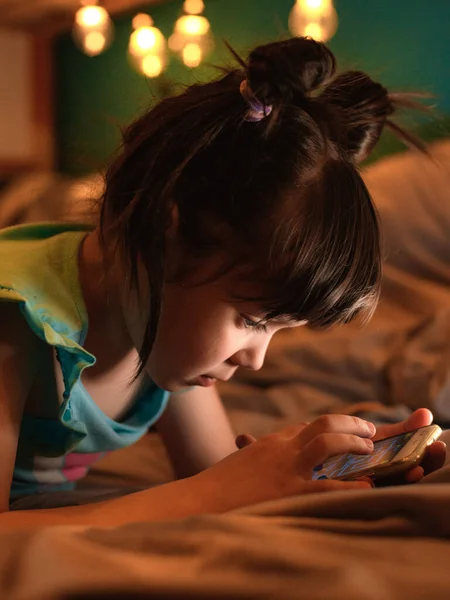 Pequena menina feliz com penteado engraçado sentado no quarto das crianças em seu beliche segurando smartphone — Fotografia de Stock