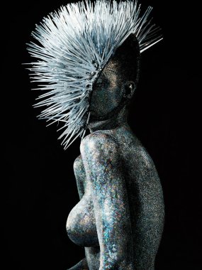 Karanlık arka planda parıltılı pozlar veren genç bir kadın.