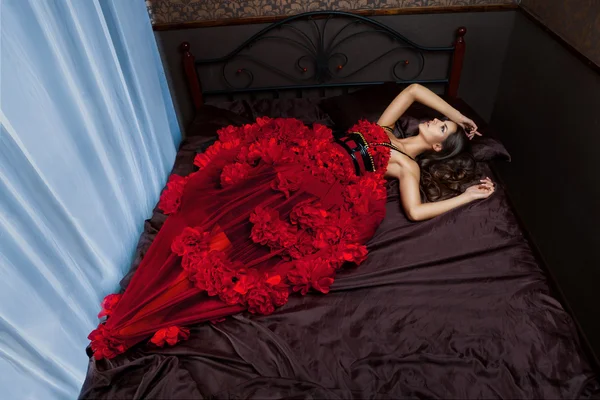 Žena v červených šatech na postel — Stock fotografie