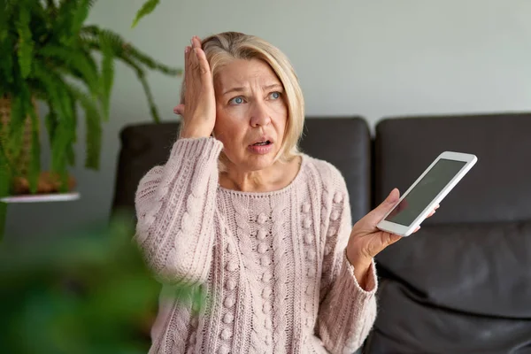 Droevige volwassen vrouw zittend op de bank en met behulp van digitale tablet. Surfen op internet via tablet thuis. — Stockfoto