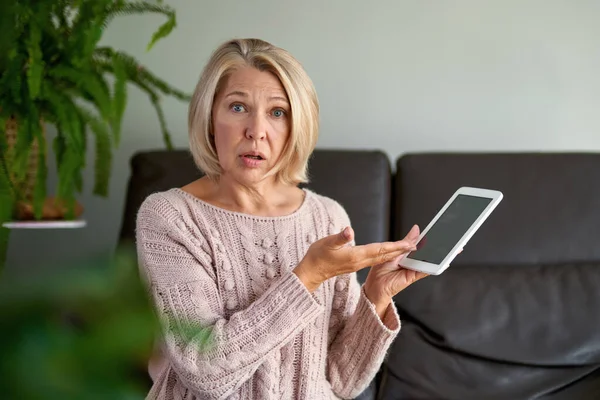Droevige volwassen vrouw zittend op de bank en met behulp van digitale tablet. Surfen op internet via tablet thuis. — Stockfoto