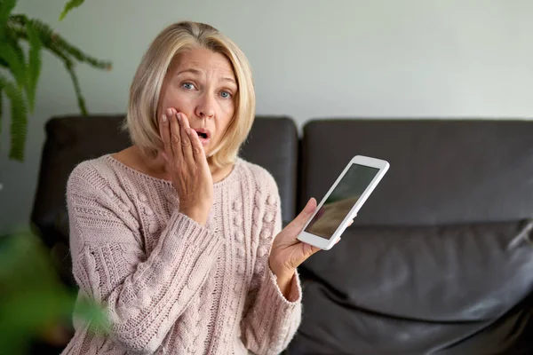 Droevige volwassen vrouw zittend op de bank en met behulp van digitale tablet. Surfen op internet via tablet thuis. — Stockfoto