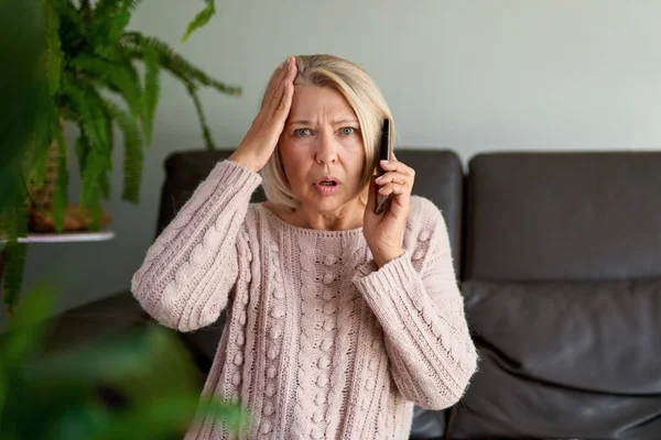 Сумна старша жінка в телефонному дзвінку сидить на дивані у вітальні — стокове фото