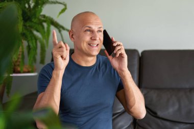 Evde akıllı telefon kullanan bir adam evdeki koltukta oturuyor.