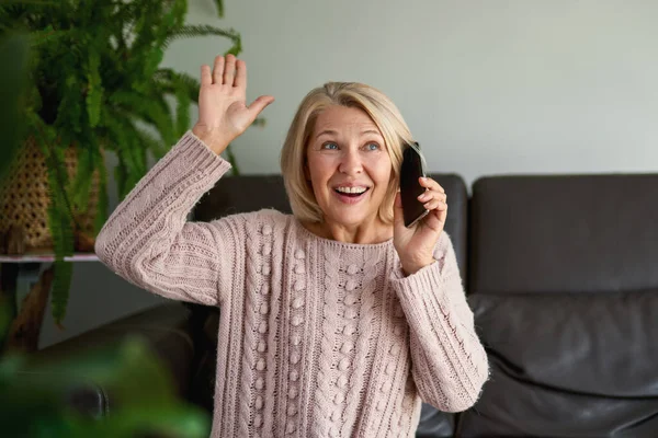 Gelukkige oudere vrouw met behulp van een telefoontje zittend op een bank in de woonkamer in een huis — Stockfoto
