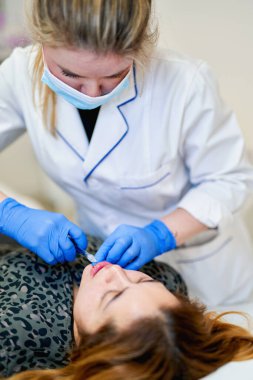 Dudak büyütme. Dudak için güzellik iğnesi yaptıran kadın. Doktor kozmetik uzmanı güzellik salonunda güzel bir kadının dudak büyütme ameliyatını yapıyor..