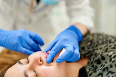 Dudak büyütme. Dudak için güzellik iğnesi yaptıran kadın. Doktor kozmetik uzmanı güzellik salonunda güzel bir kadının dudak büyütme ameliyatını yapıyor..