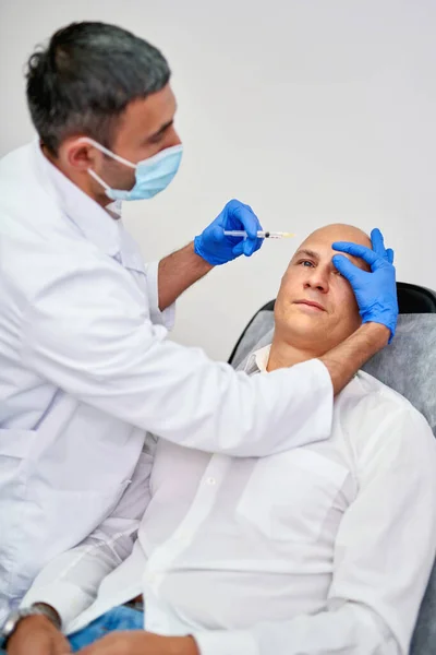 Cosmetologist making botox injection. Holding syringe. Man is receiving procedure with enjoyment