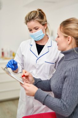 Nüfusun toplu aşılanması. Maskeli kadın doktor, Covid-19 antiviral aşıyı vermeden önce hastaya imzalaması için belgeler veriyor.