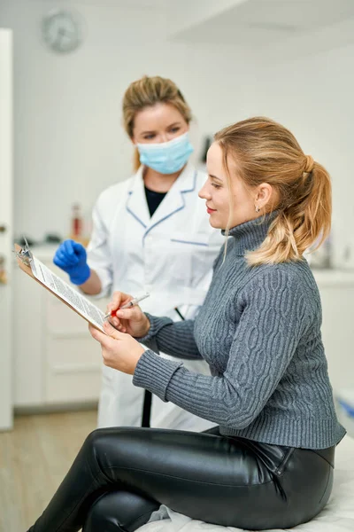 Hromadné očkování populace. Ženský lékař v masce dává pacientce dokumenty k podpisu před podáním antivirové vakcíny Covid-19 — Stock fotografie