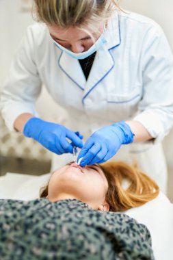 Dudak büyütme. Dudak için güzellik iğnesi yaptıran kadın. Doktor kozmetik uzmanı güzellik salonunda güzel bir kadının dudak büyütme ameliyatını yapıyor..