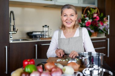 Mutfakta kıdemli bir kadın yemek pişiriyor, tencerede yemek pişiriyor.