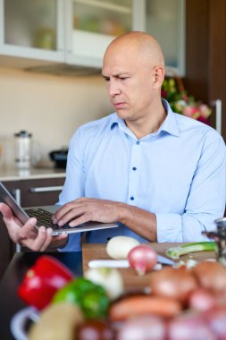 Mutfakta dizüstü bilgisayarında yemek tarifi arayan bir adam var. Evde yemek yapmak, internetten..