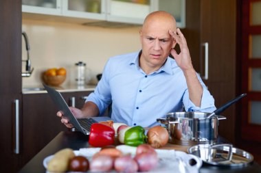 Tabletteki tarifin yardımıyla üzgün adam yemek pişiriyor..