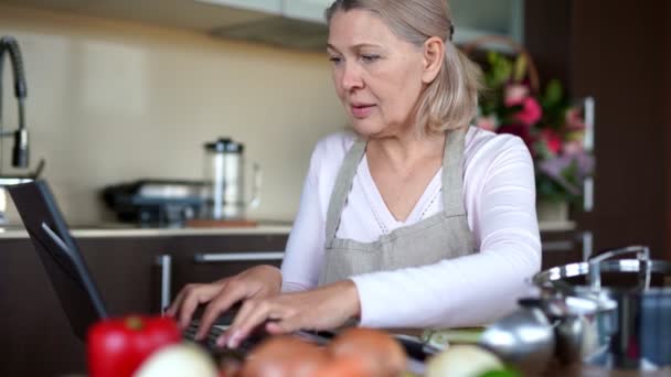 Starsza kobieta gotowanie z pomocą receptury na laptopie. — Wideo stockowe