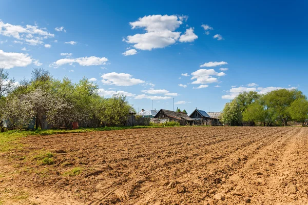 Plowed field on a background of rural houses — Stock Photo, Image