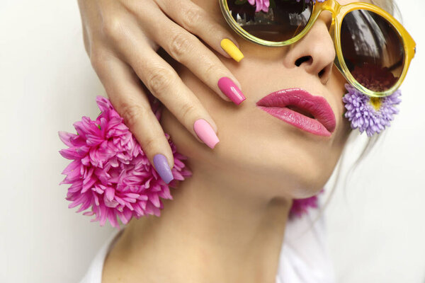 Fashionable multi-colored makeup and manicure on long nails of a girl with asters and glasses.