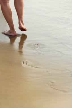 A man walks on a wet sandy beach .